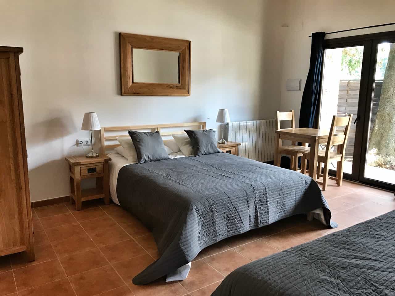 Hotel bedroom with a double bed, wooden furniture, and glass doors leading to an outdoor area in Girona.