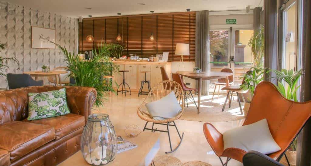 Modern hotel lounge with leather sofa, rattan chairs, potted plants, and wooden bar area.