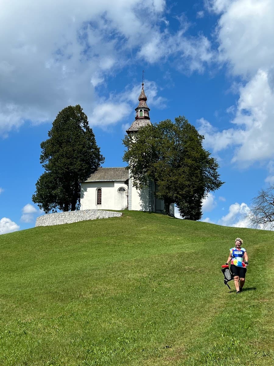 Hiker ascending grassy hill towards white church with steeple under blue, cloudy sky