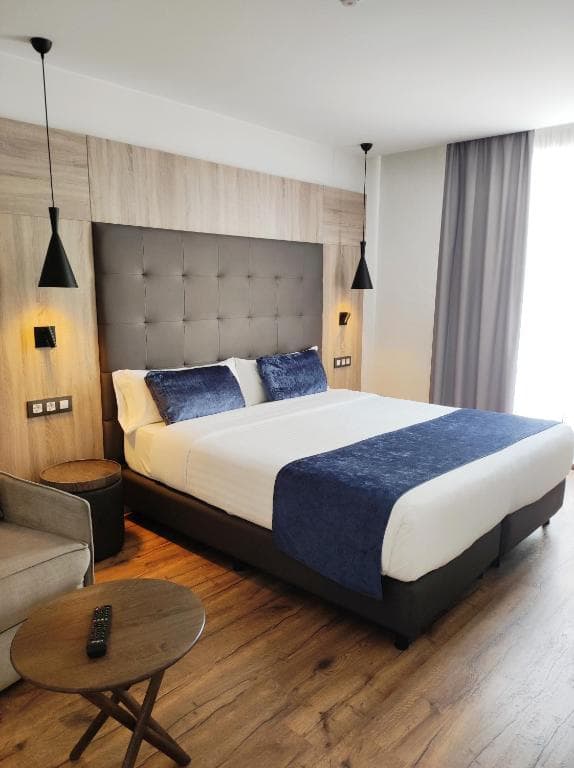 Modern hotel room with a queen bed, blue velvet pillows, and wooden bedside tables.