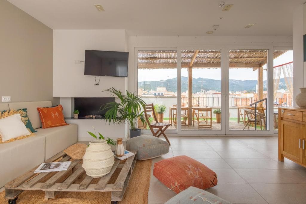 Modern living room with pallet coffee table, sofa, and terrace overlooking a town with mountains in the background.