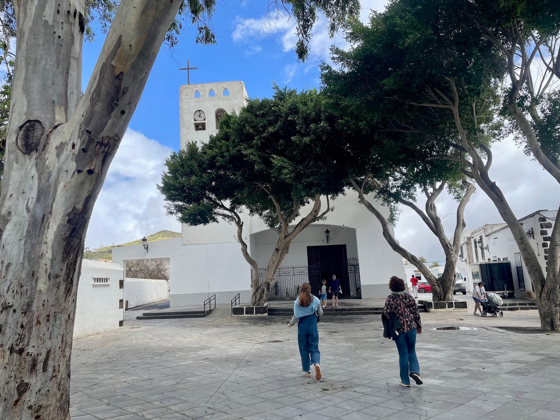 People walking across a plaza toward a white church with a bell tower in Lanzarote.