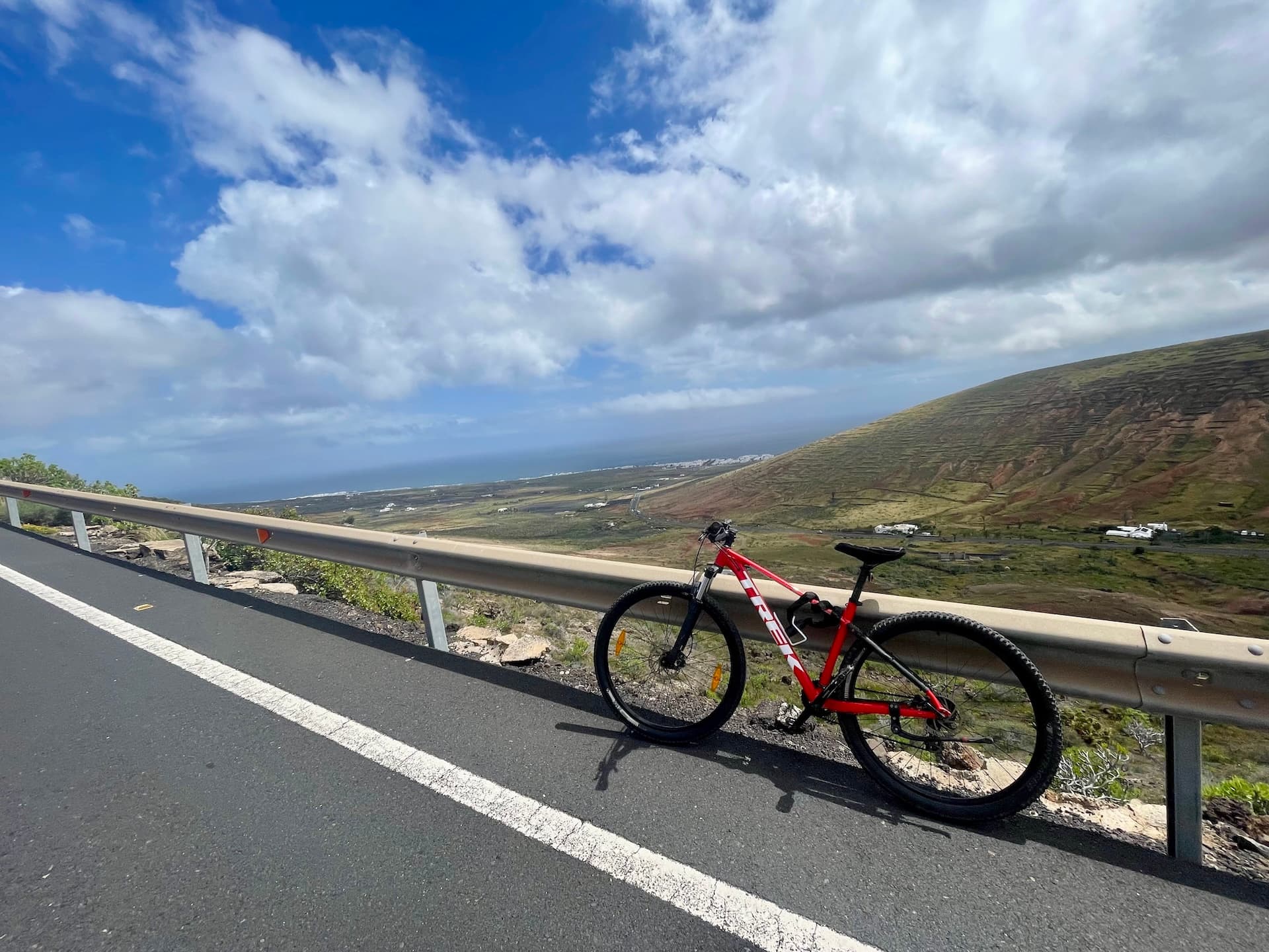 Red mountain bike parked by a guardrail overlooking a volcanic landscape and the coastline in Lanzarote.