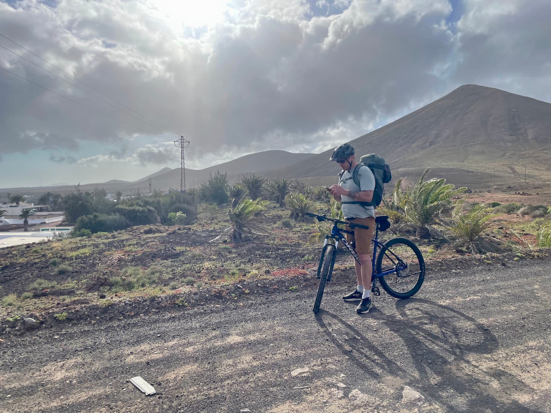 Cyclist with backpack standing on a dirt path in Lanzarote with volcanic mountains in the background.