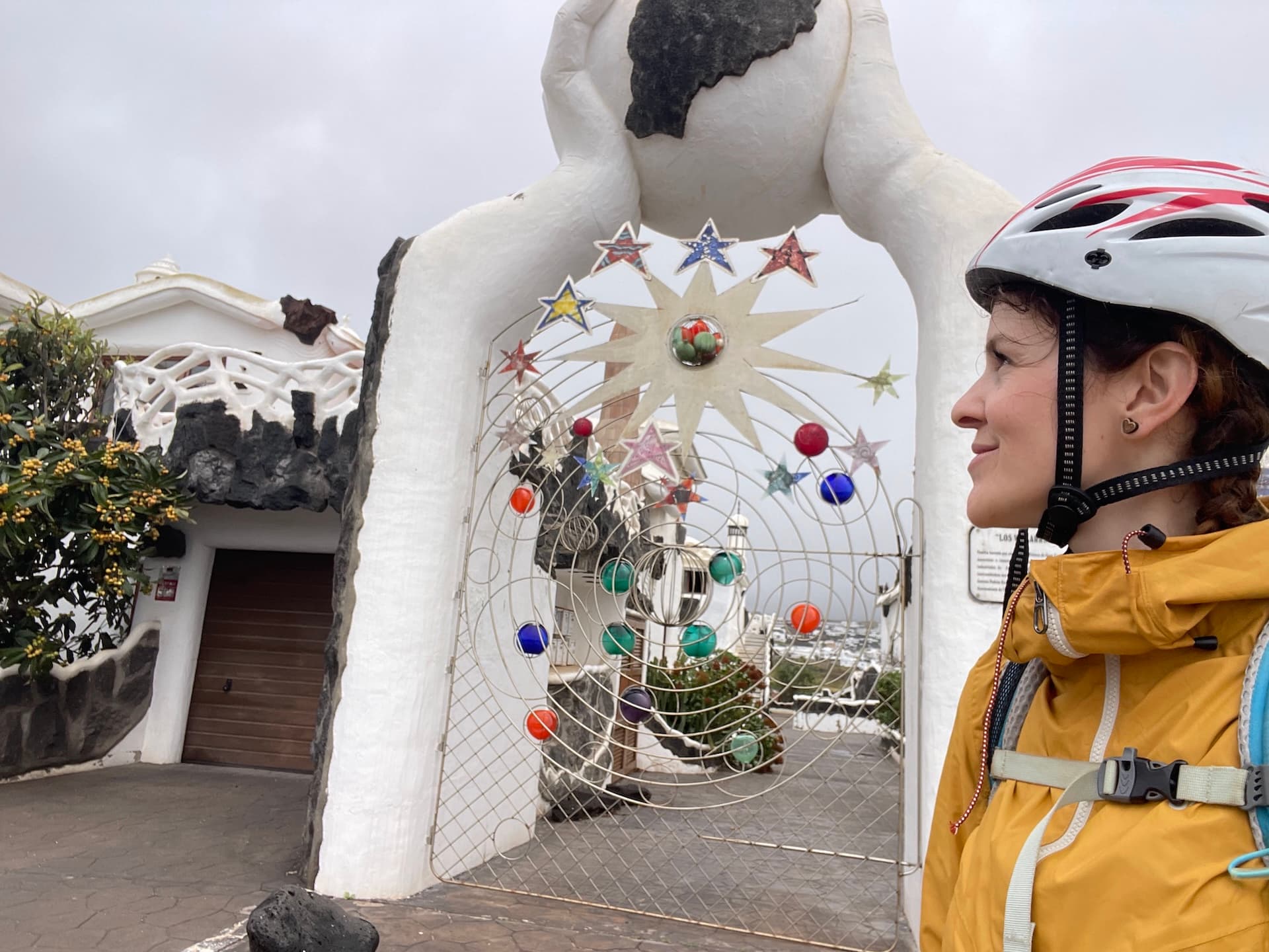 Cyclist wearing a helmet standing before an ornate gate with star and planet decorations in Lanzarote.