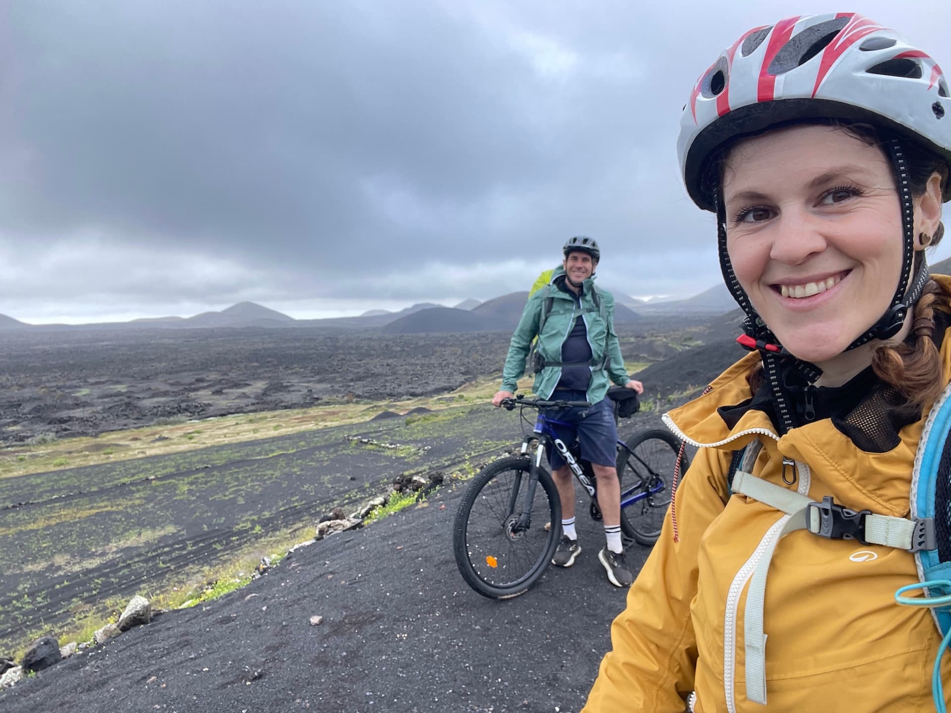 Two cyclists in helmets posing for a selfie on a volcanic landscape in Lanzarote.