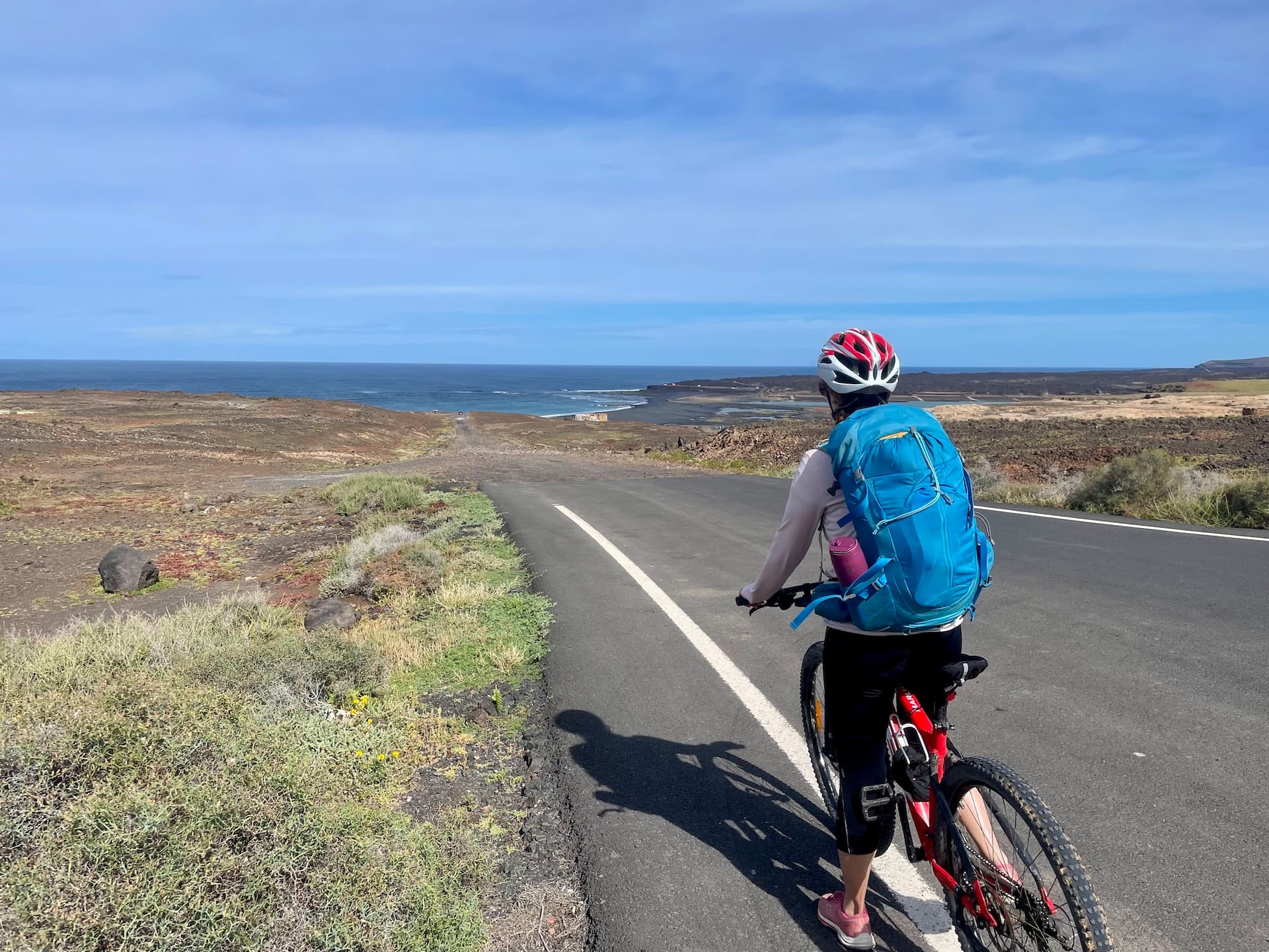 Cyclist with blue backpack on a paved road leading toward the coast in Lanzarote.