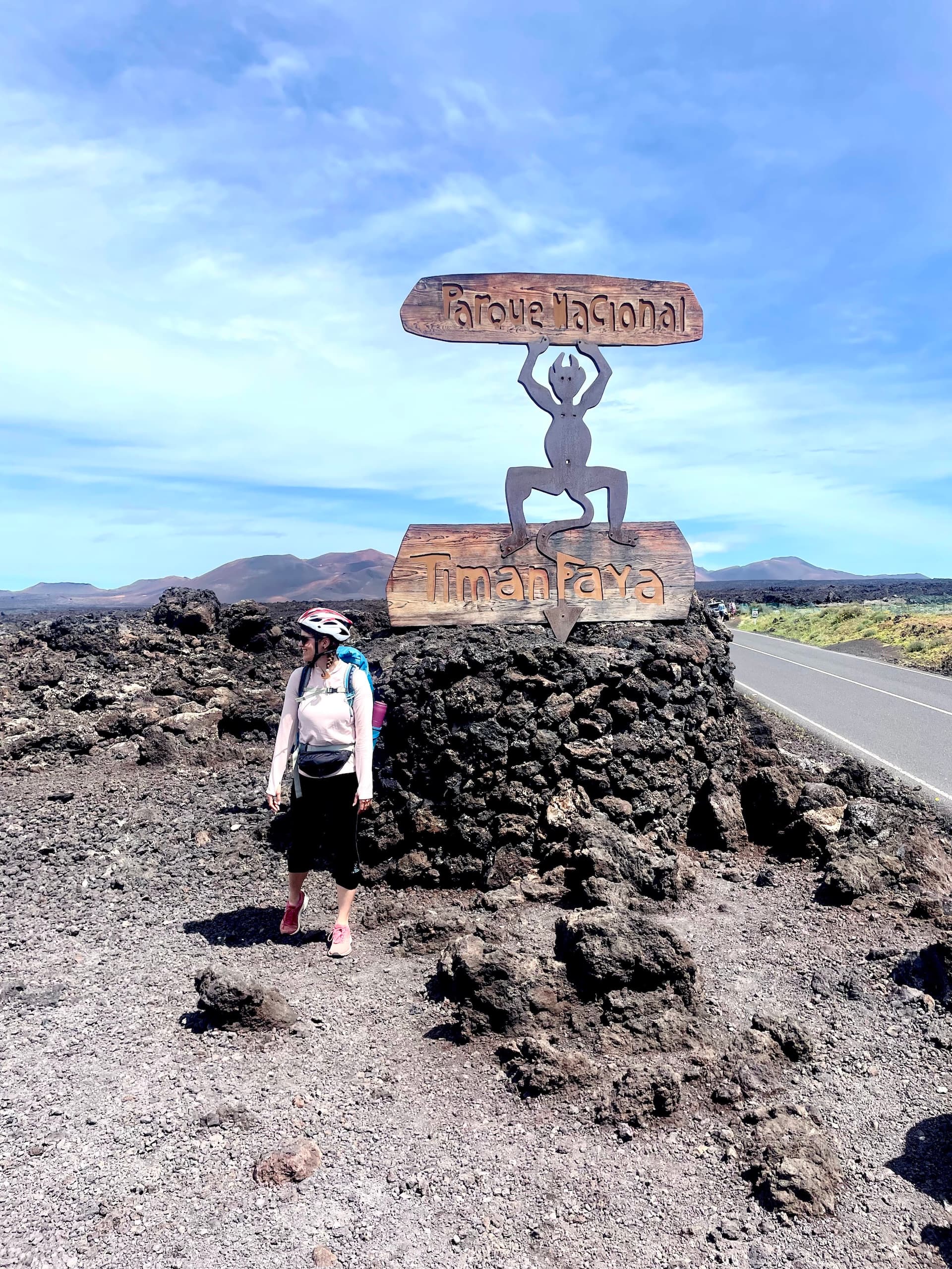 Cyclist standing by the Timanfaya National Park sign in a volcanic landscape in Lanzarote.