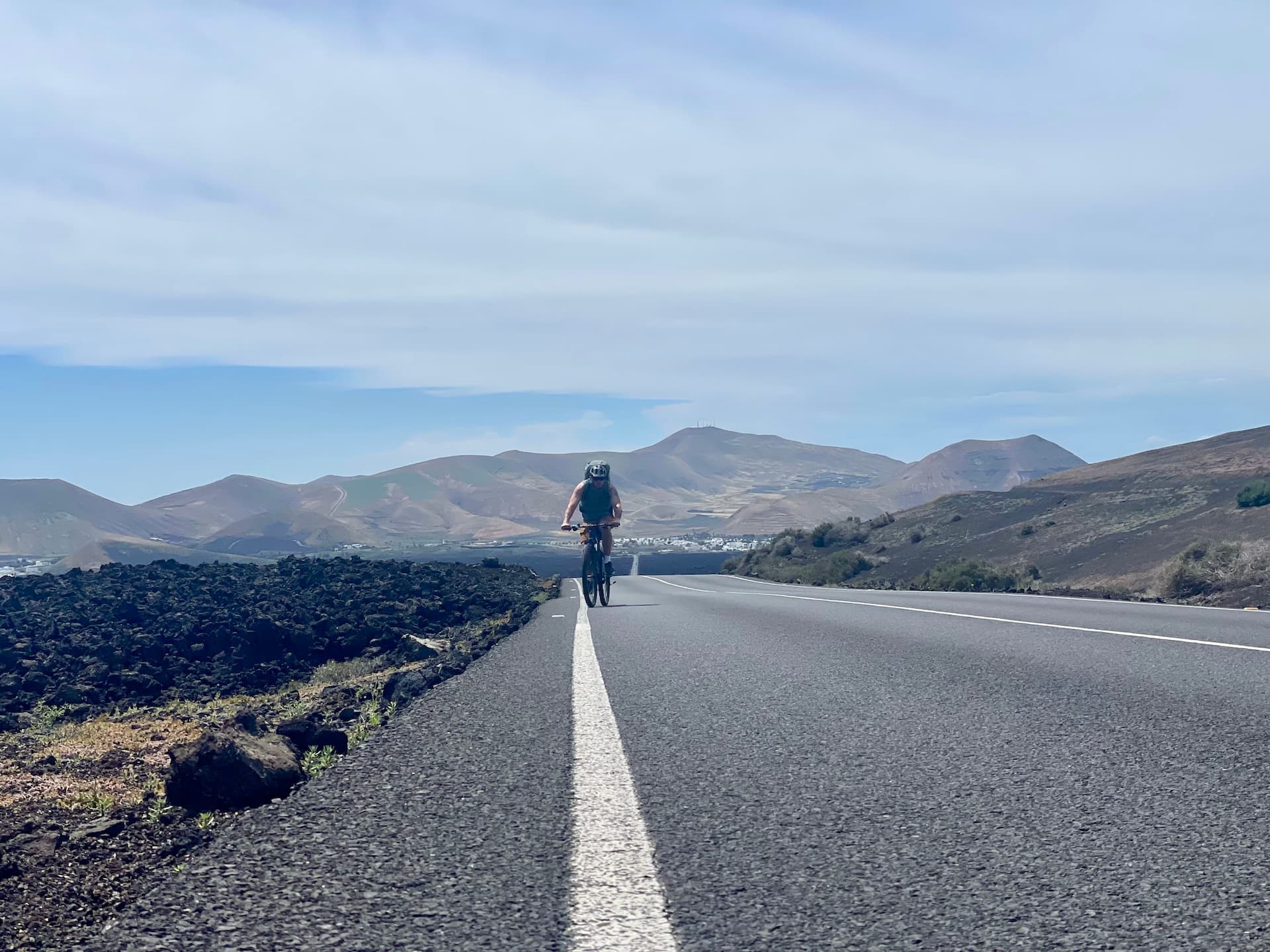 Cyclist riding on a paved road through a volcanic landscape in Lanzarote.
