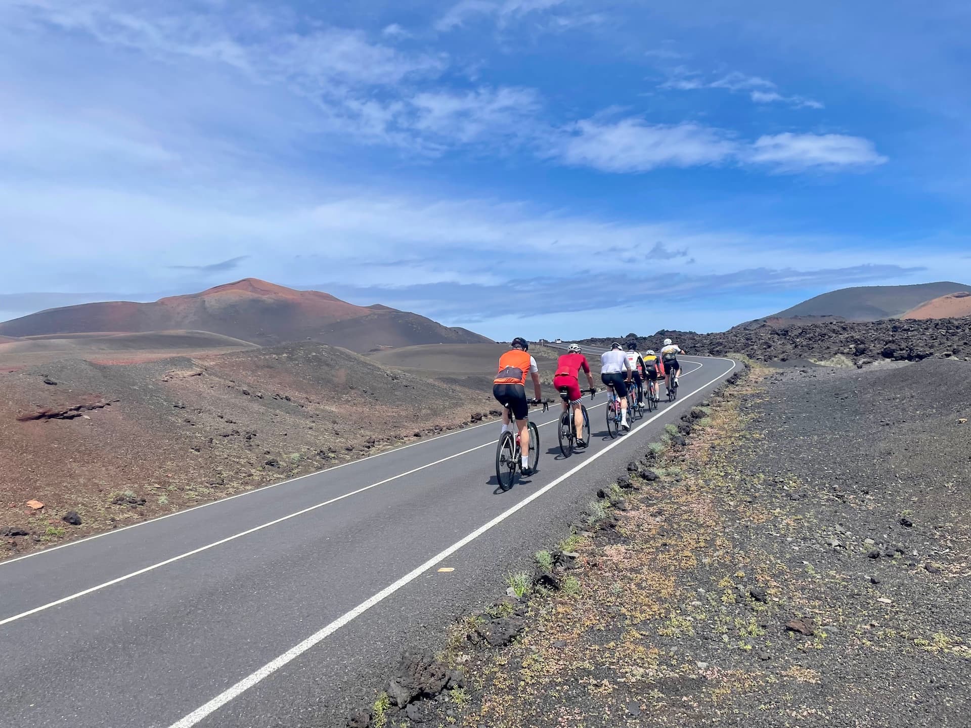 Cyclists riding on a paved road through a volcanic landscape in Lanzarote.