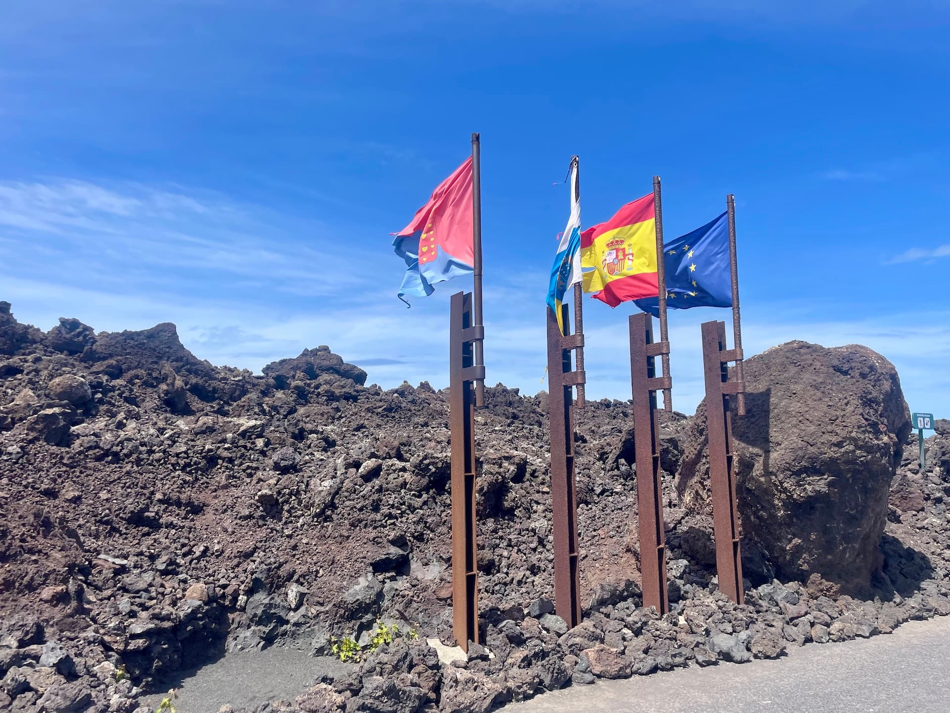 Flags including the Spanish and European Union flags flying over a volcanic rock landscape in Lanzarote.