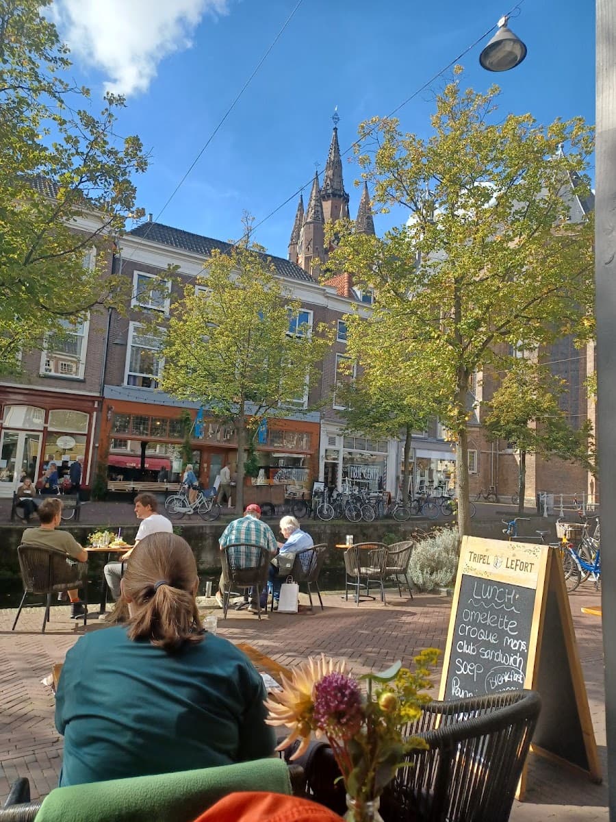 Outdoor cafe dining along a canal with historic European buildings and church spires