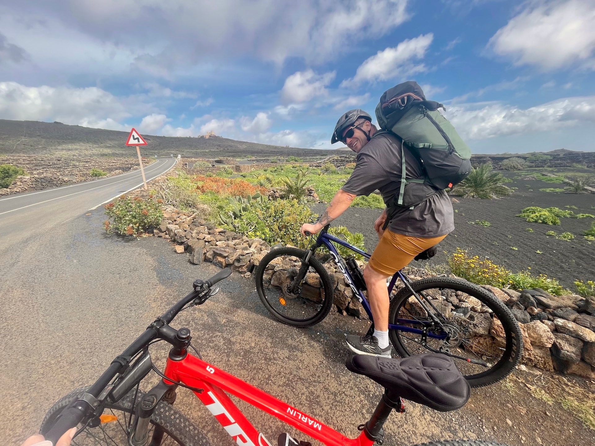 Cyclist with backpack riding a mountain bike on a road through a volcanic landscape in Lanzarote.