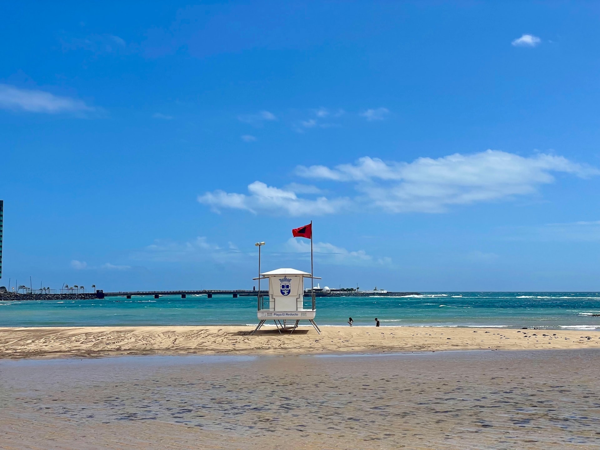 Lifeguard tower with red flag on Playa El Reducto beach in Lanzarote with turquoise sea and blue sky.