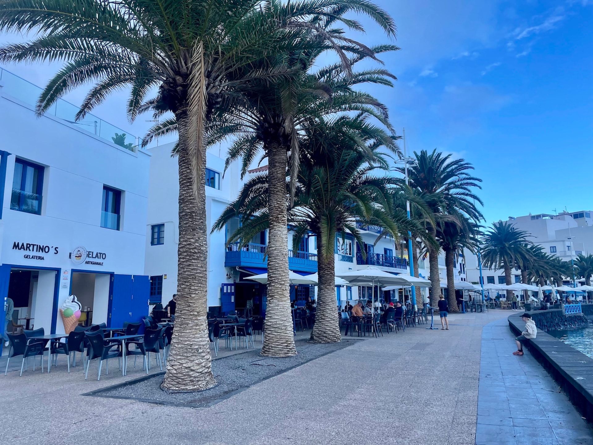 Outdoor cafe seating with palm trees along a waterfront promenade in Lanzarote.
