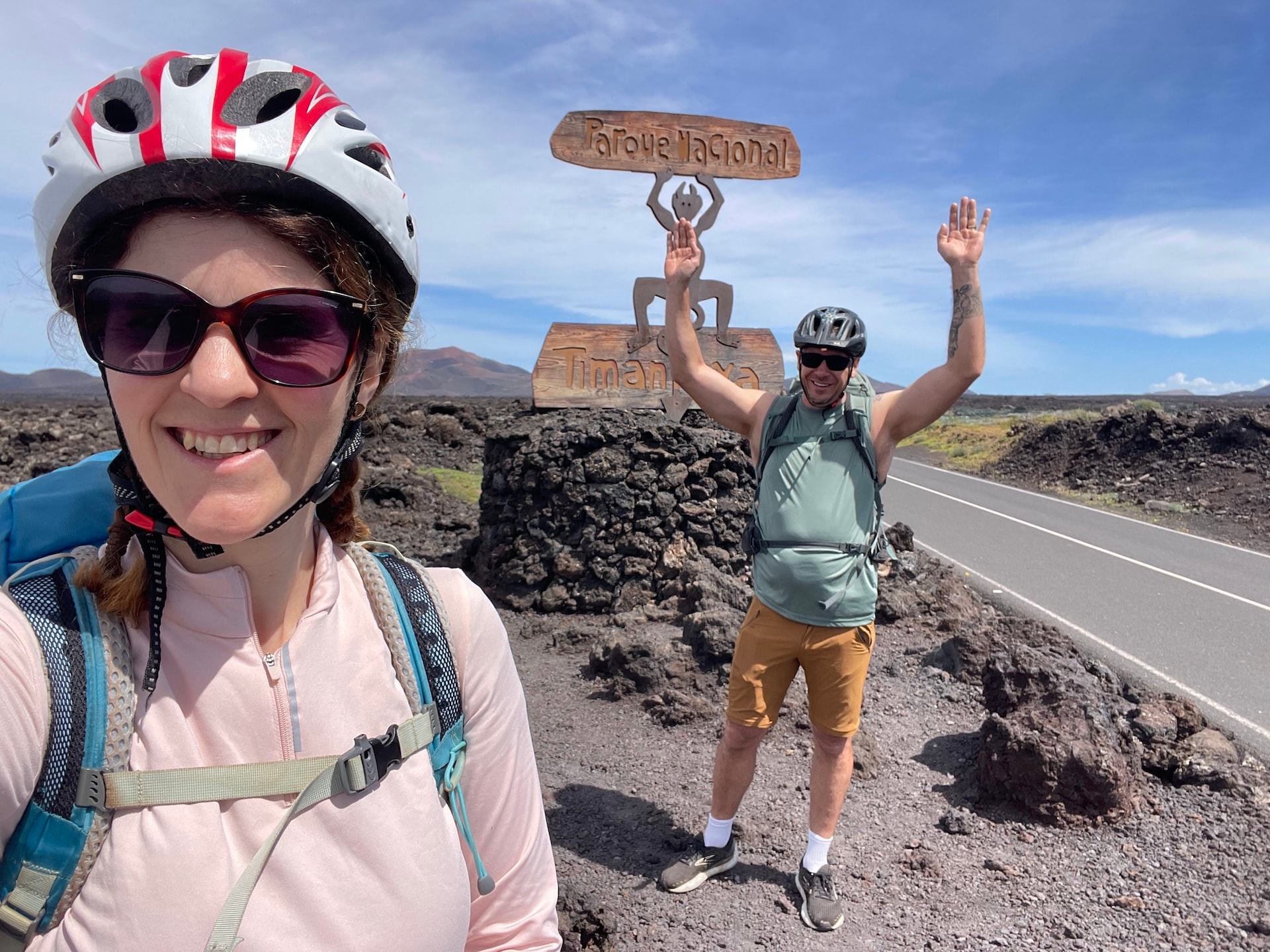 Cyclists posing by the Timanfaya National Park sign in Lanzarote with volcanic landscape.