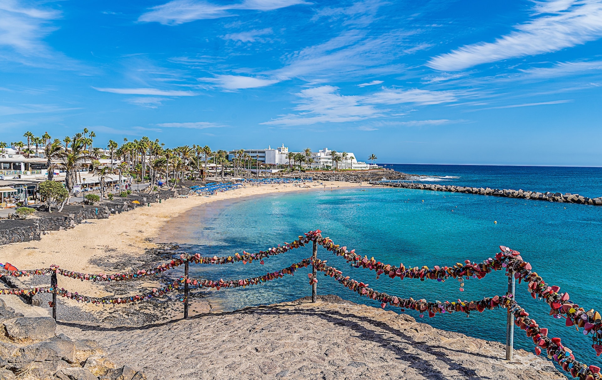 Love locks on a metal fence overlooking a sandy beach and turquoise water in Lanzarote, Canary Islands.