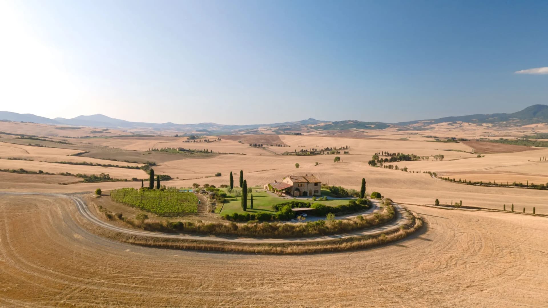 Farmhouse on green oasis surrounded by rolling golden fields in Val d'Orcia.