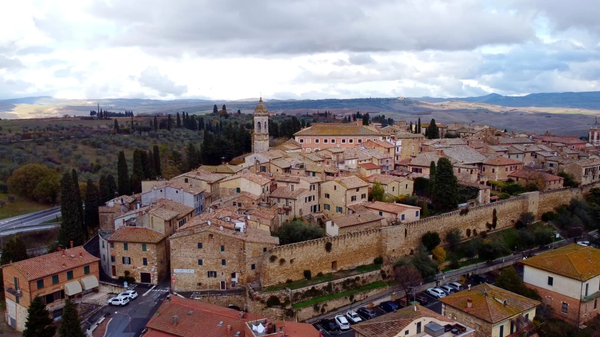 Hilltop town of San Quirico d'Orcia with stone walls, terracotta roofs, and rolling Tuscan countryside.