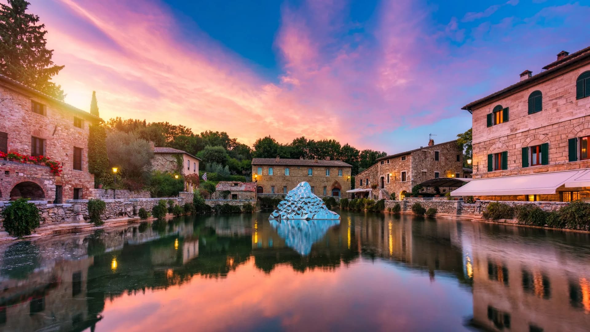 Thermal pool with stone buildings and modern sculpture at sunset in Bagno Vignoni.