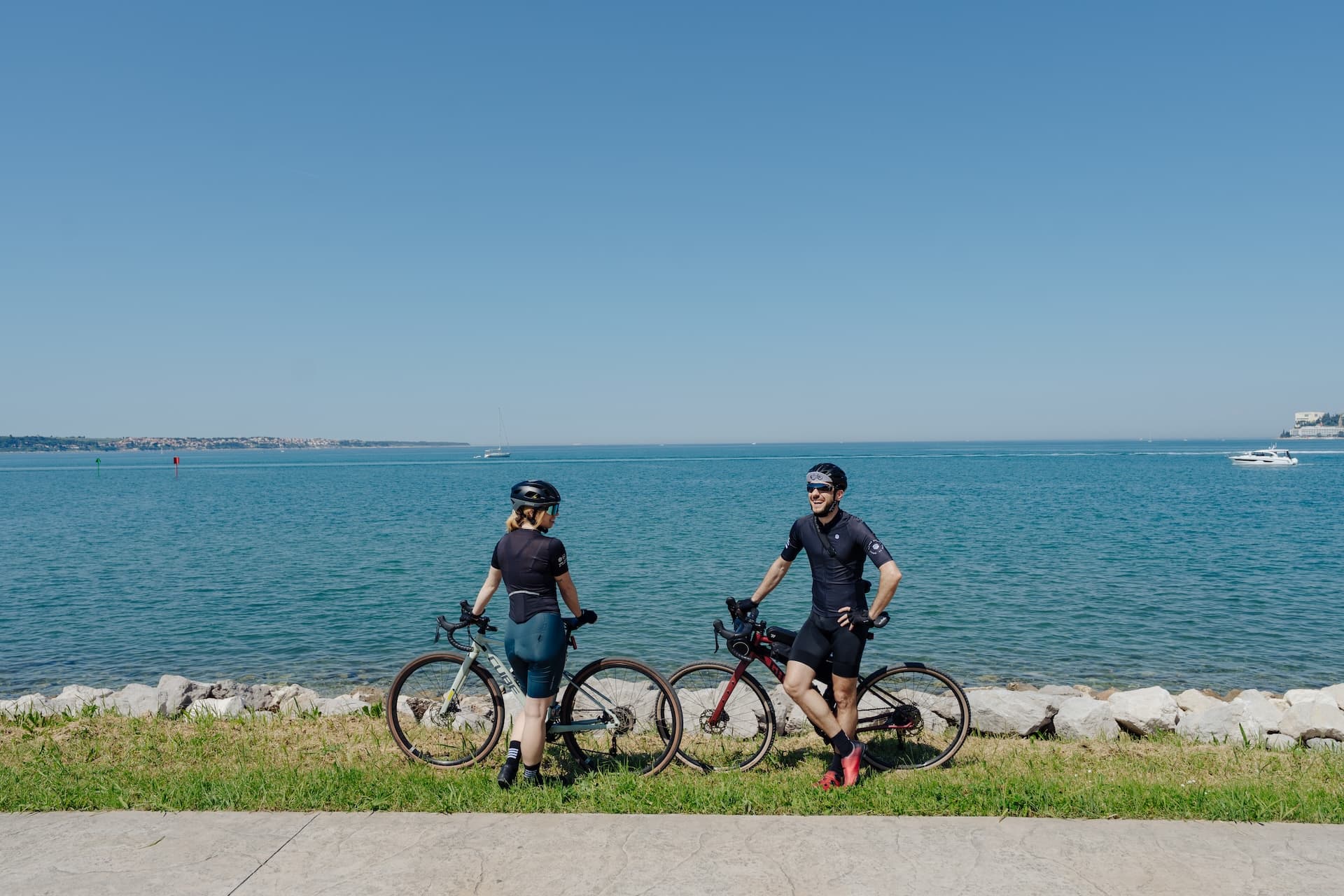 Cyclists resting with bikes by the sea with a distant Croatian coastline and boats.