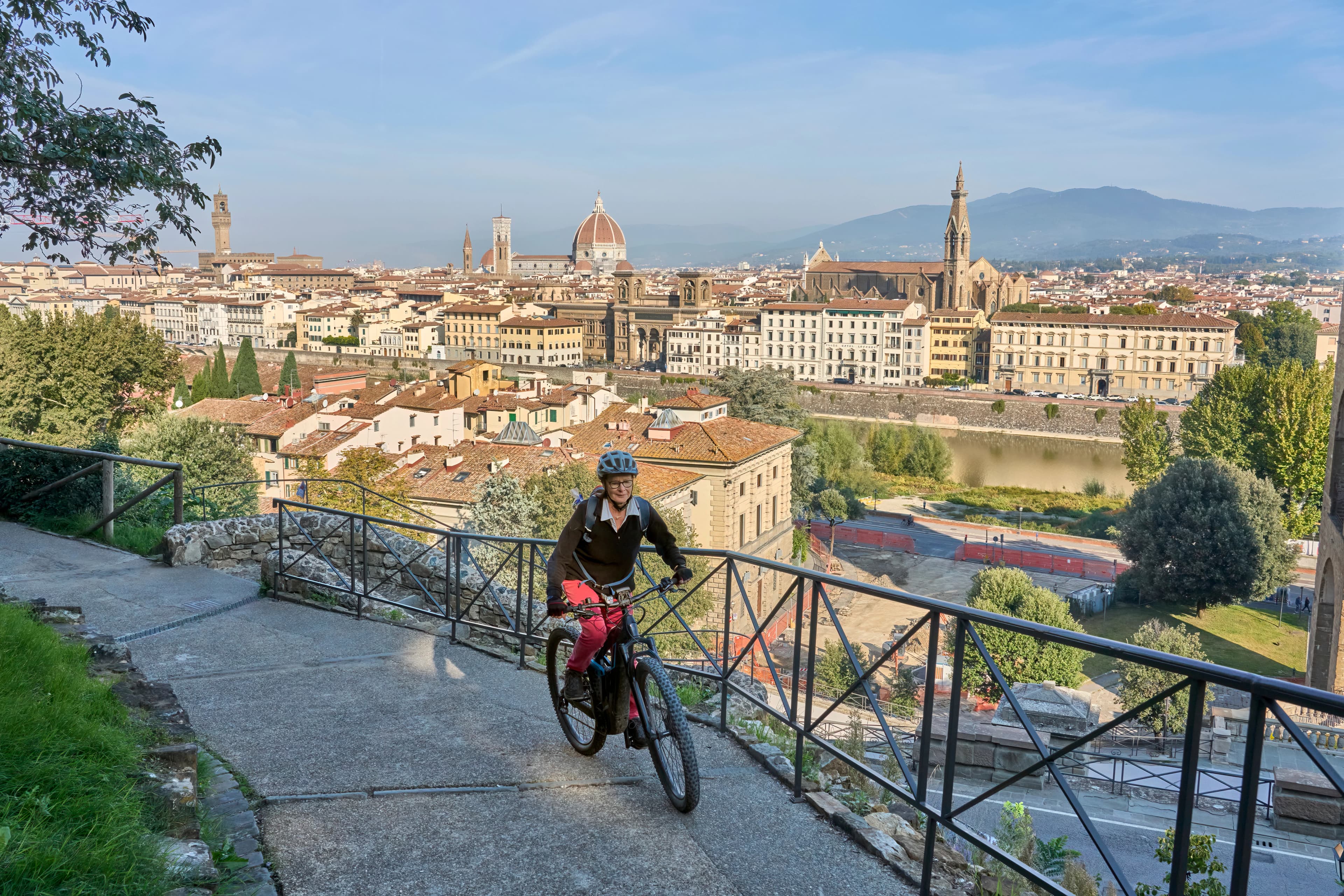cheerful senior woman cycling with her electric mountain bike above downtown of Florence with stunning view over the old city, Tuscany, Italy