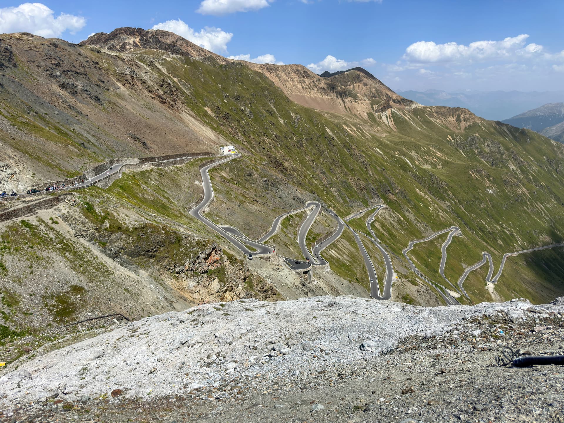 A panoramic view of the winding mountain roads of the famous Stelvio Pass, set against a backdrop of majestic peaks and a cloudy sky.