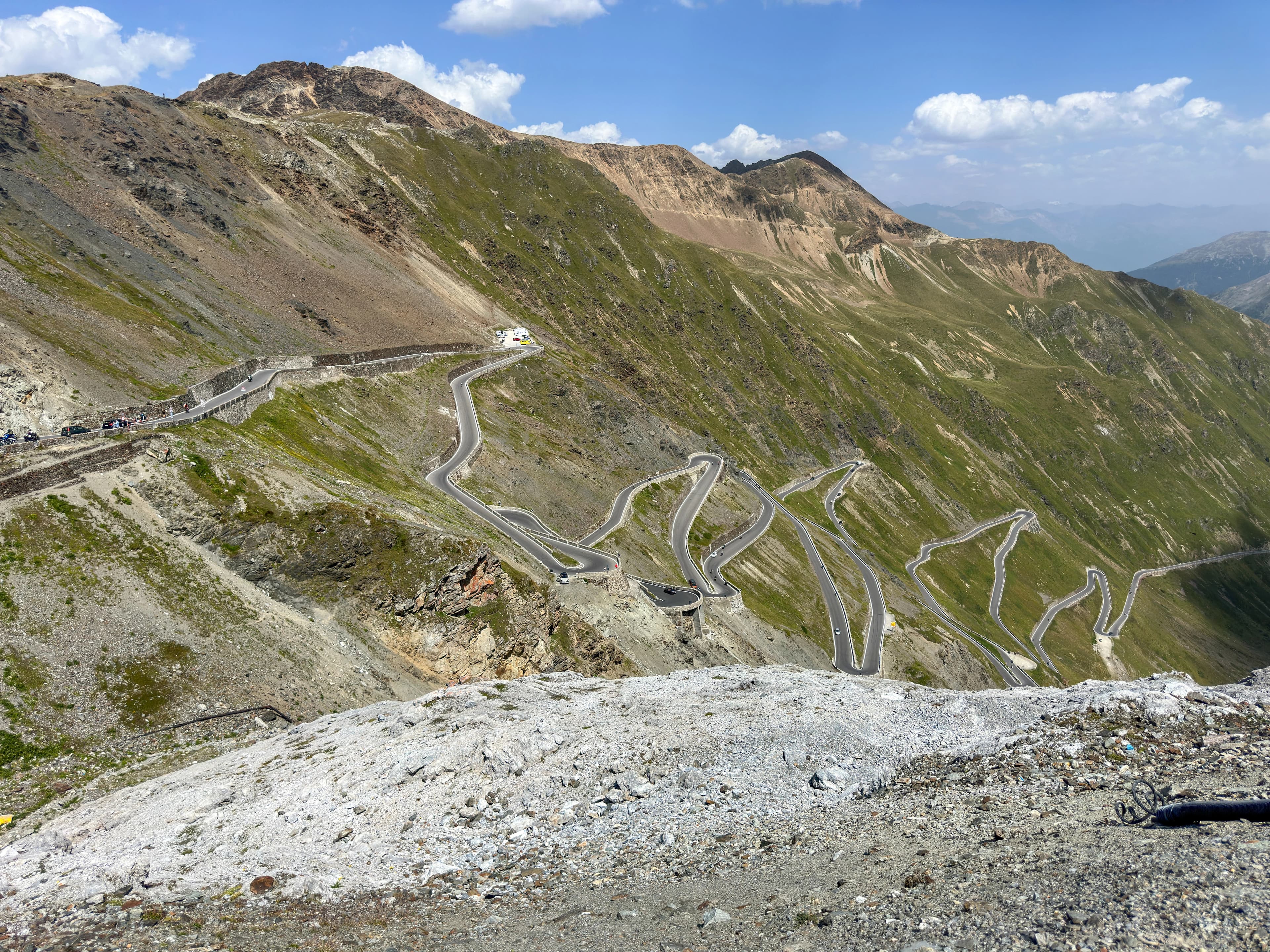 A panoramic view of the winding mountain roads of the famous Stelvio Pass, set against a backdrop of majestic peaks and a cloudy sky.