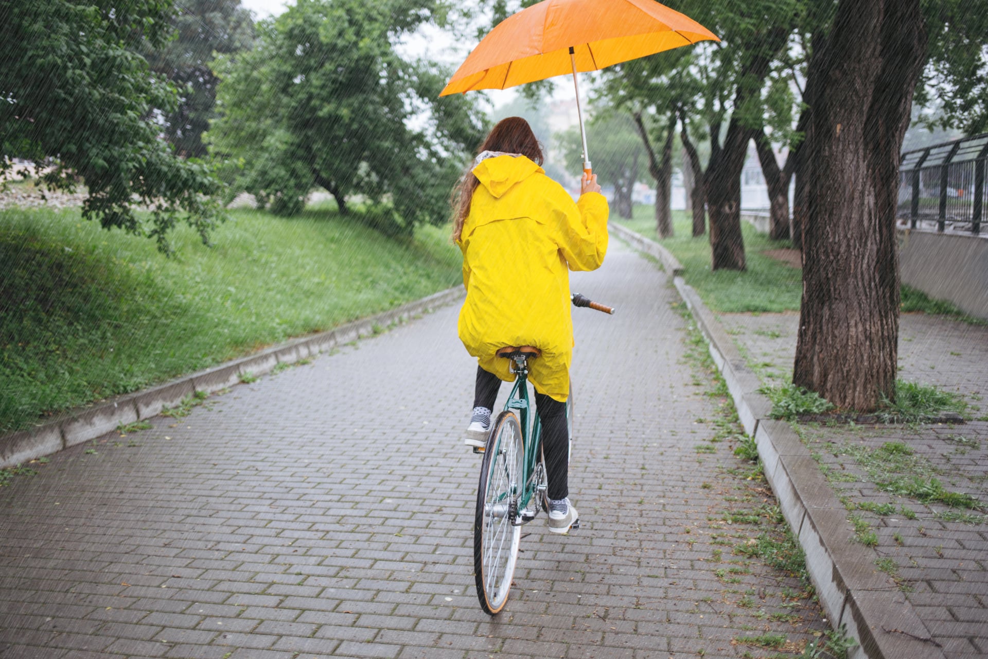 Rear view of bicycle rider wearing raincoat while cycling with umbrella