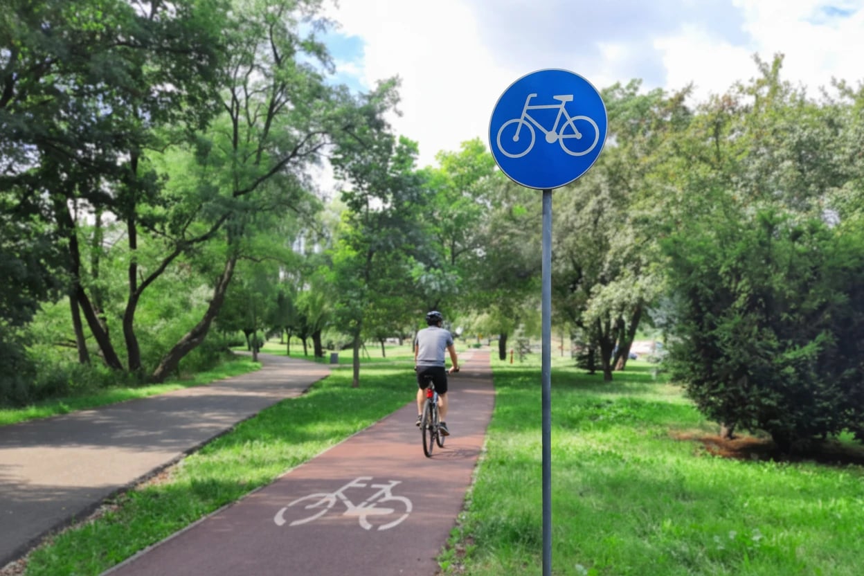 Bicycle path in a summer city park. Bike lane sign. Traffic sign white bicycle on blue circle and road markings on the asphalt. Concept of infrastructure development for ecological transport.