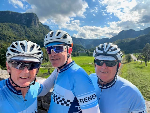 Cyclists in matching blue jerseys and helmets with mountain backdrop